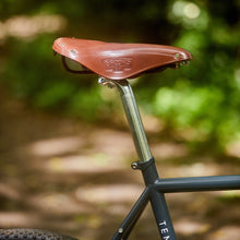 Load image into Gallery viewer, Brown bicycle saddle with 'Brooks' branding on a blurred natural background
